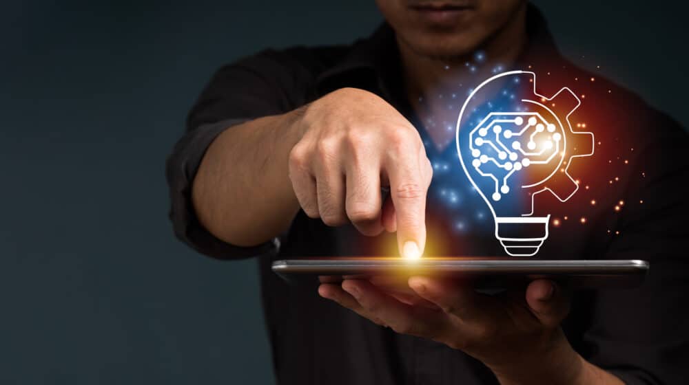 A businessman shows a cost-effectiveness of video training concept by holding half of a virtual lightbulb and his brain on a digital tablet.